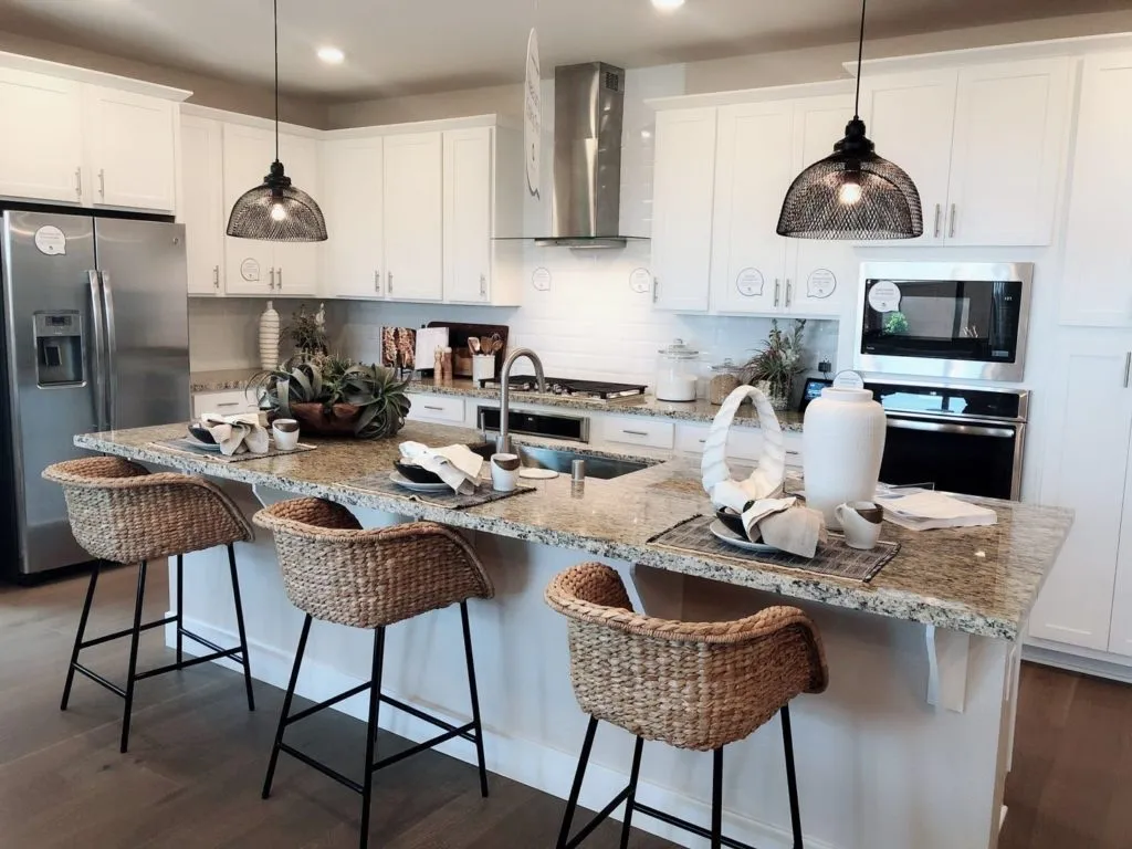 White kitchen with granite island, woven stools and black pendant lights